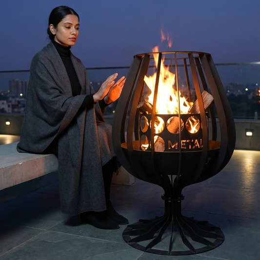 Person sitting by a large metal fire pit on a rooftop at night.