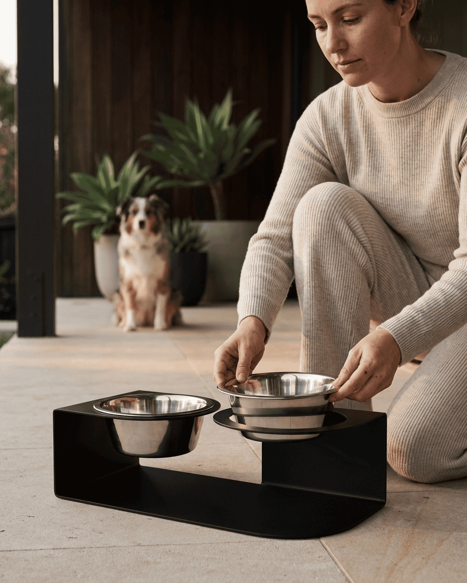 Woman setting up a black elevated pet feeder with two bowls on a wooden deck.
