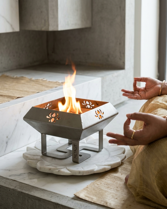 Small havan kundwith flames on a marble surface, person meditating in the background. metalit hawan kund with satiya on the base